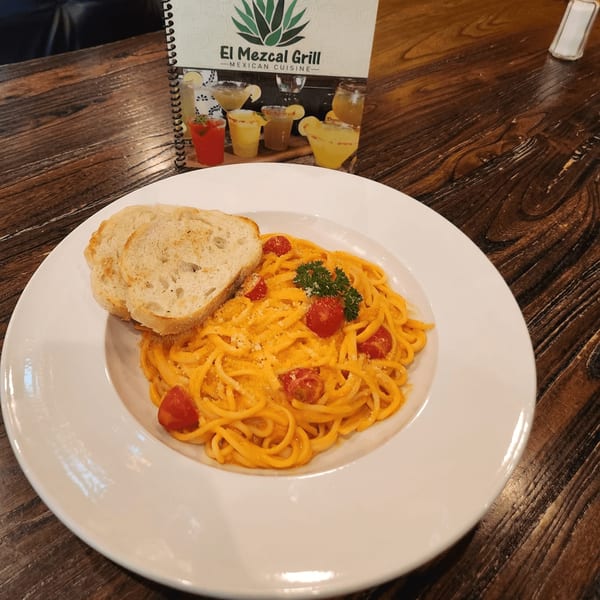 Pasta with creamy orange sauce, cherry tomatoes, and bread slices on a white plate at El Mezcal Grill.