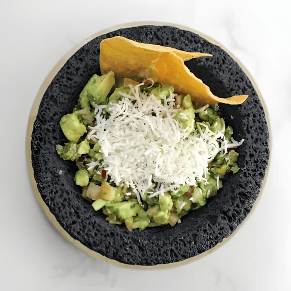 El Mezcal Grill's guacamole with shredded cheese and a tortilla chip in a dark bowl.
