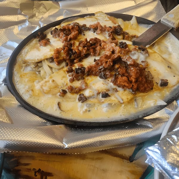 A sizzling skillet of El Mezcal Grill's melted cheese with chorizo and onions, served with a spatula.