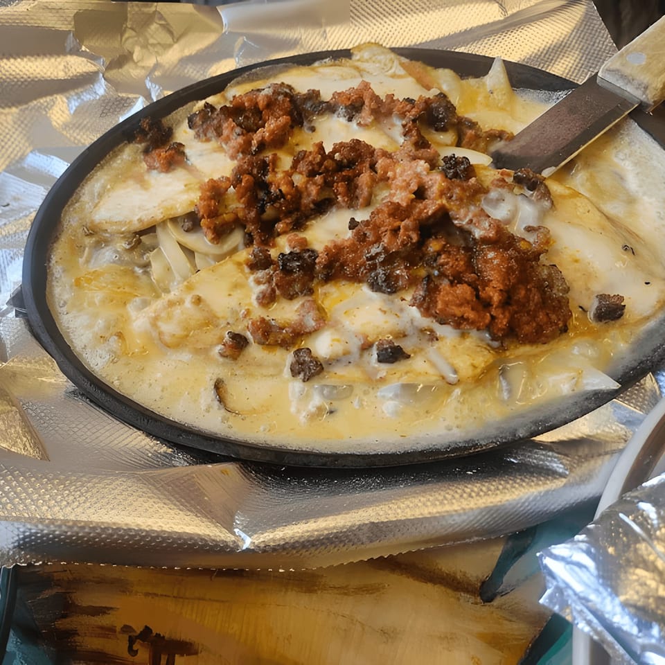 A sizzling skillet of El Mezcal Grill's melted cheese with chorizo and onions, served with a spatula.