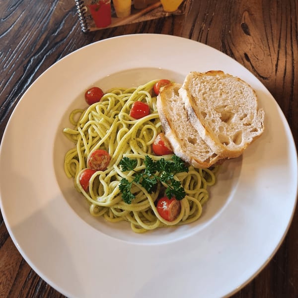 Green pesto spaghetti with cherry tomatoes, parsley, and two slices of bread on a white plate.